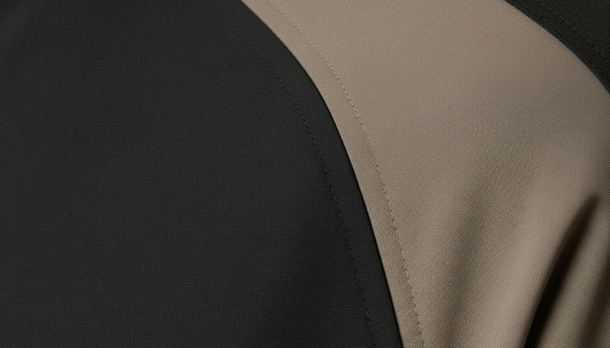 Gros plan sur l'épaule : la couture raglan entre le corps noir et la manche taupe.