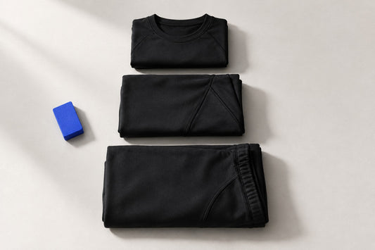 Trois vêtements noirs pliés et empilés par taille croissante, à côté d'un bloc de craie de tailleur bleu.