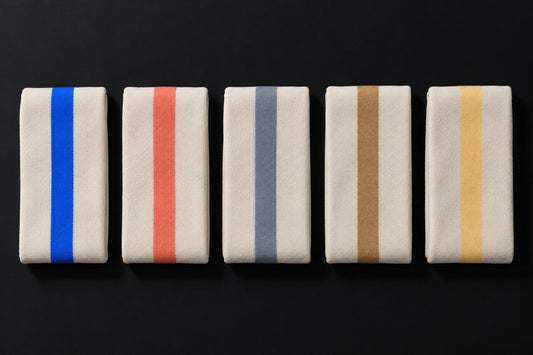 Cinq pièces en maille écrue pliées et alignées, chacune portant une seule bande d'une couleur d'accent différente.
