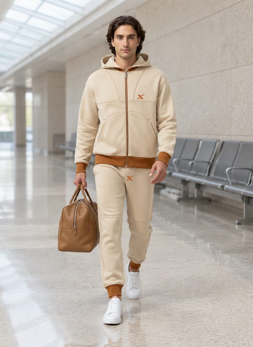 The model walks through an airport corridor, bag in hand, dressed in the Grid Stitch Hooded Set.